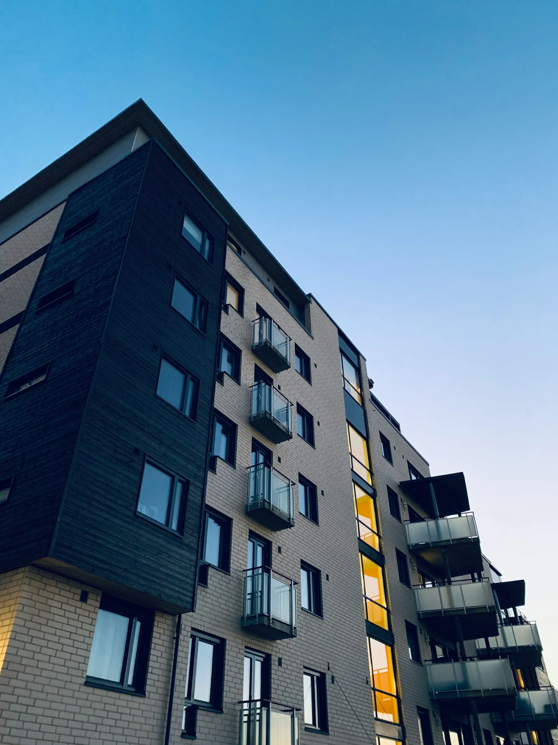 Edifício residencial de fachada clara com sacadas envidraçadas, visto de baixo ao entardecer